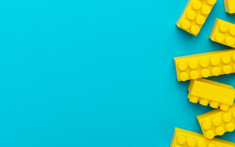 An image of yellow lego bricks scattered on the right hand side of a bright blue background.